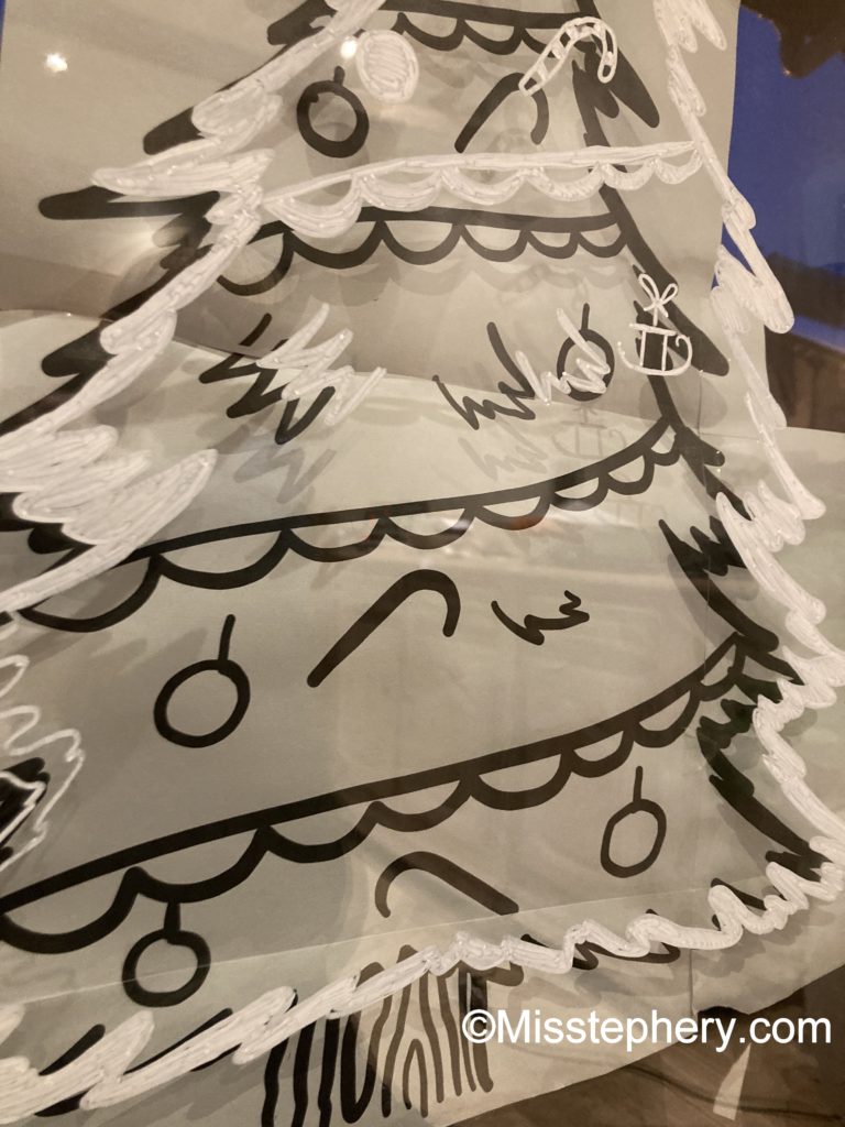 Technique pour décalquer un dessin de Noël sur une vitre : le modèle papier est visible sous le tracé au feutre Posca blanc. Illustration de la méthode anti-flou.