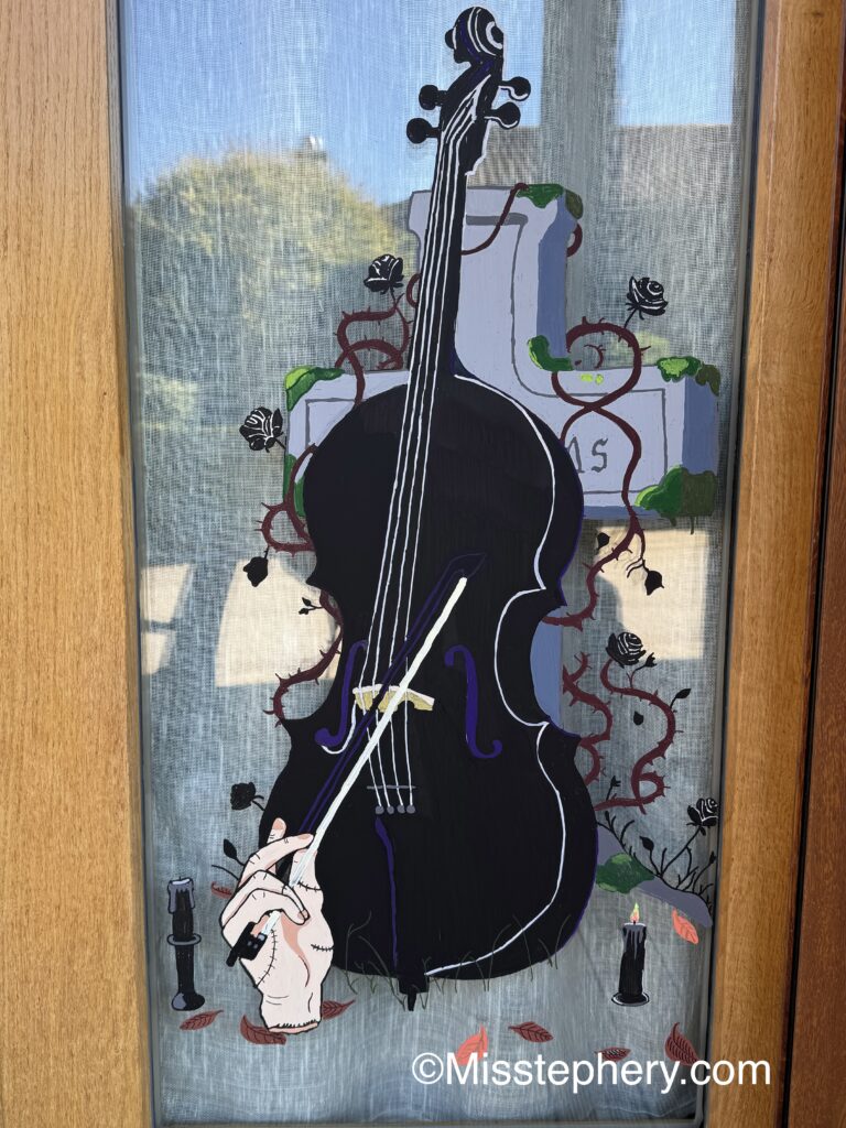 Dessin au Posca sur vitre du violoncelle de Mercredi Addams avec la main La Chose et une tombe pour Halloween
