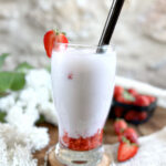 Ddalgi Latte Vegan aux fraises fraîches et lait de cajou sans lactose présenté dans un verre tulipe sur un rondin de bois.