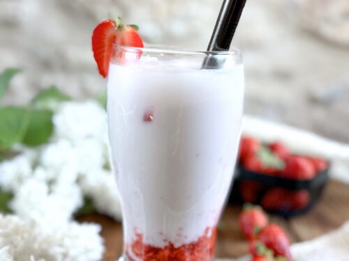 Ddalgi Latte Vegan aux fraises fraîches et lait de cajou sans lactose présenté dans un verre tulipe sur un rondin de bois.
