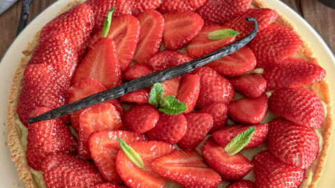 Tarte aux fraises fraîche décorée de menthe et gousse de vanille sur table en bois rustique