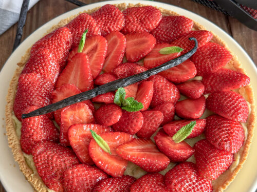 Tarte aux fraises fraîche décorée de menthe et gousse de vanille sur table en bois rustique
