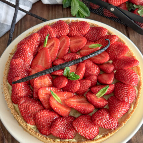 Tarte aux fraises fraîche décorée de menthe et gousse de vanille sur table en bois rustique
