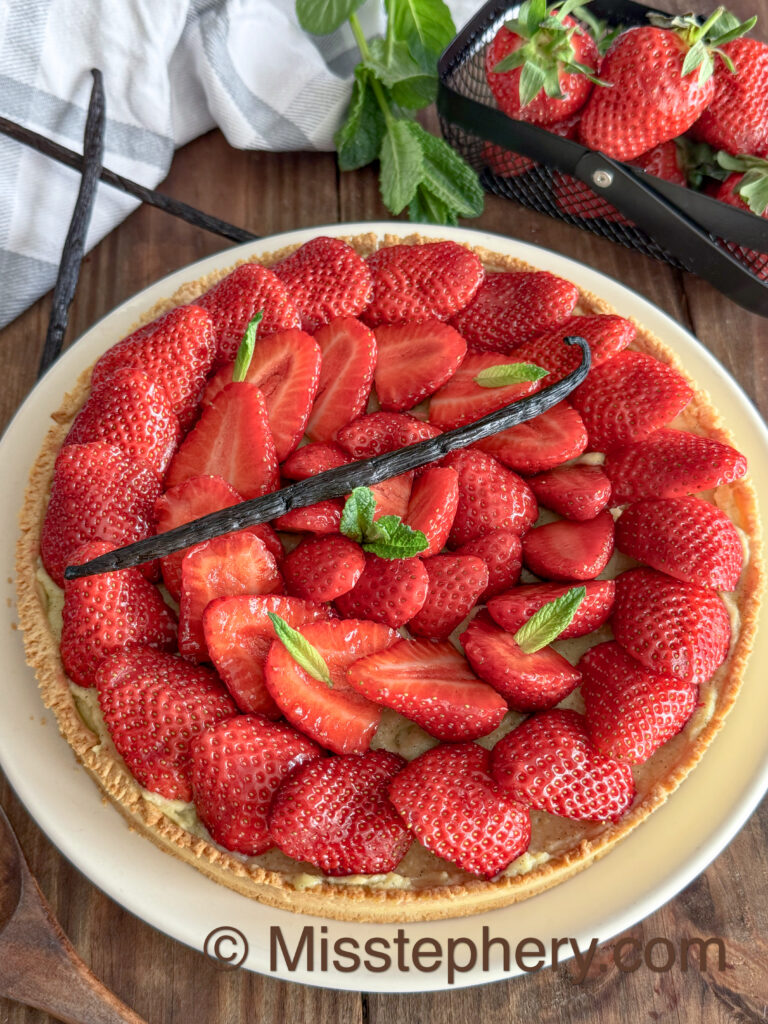 Tarte aux fraises fraîche décorée de menthe et gousse de vanille sur table en bois rustique