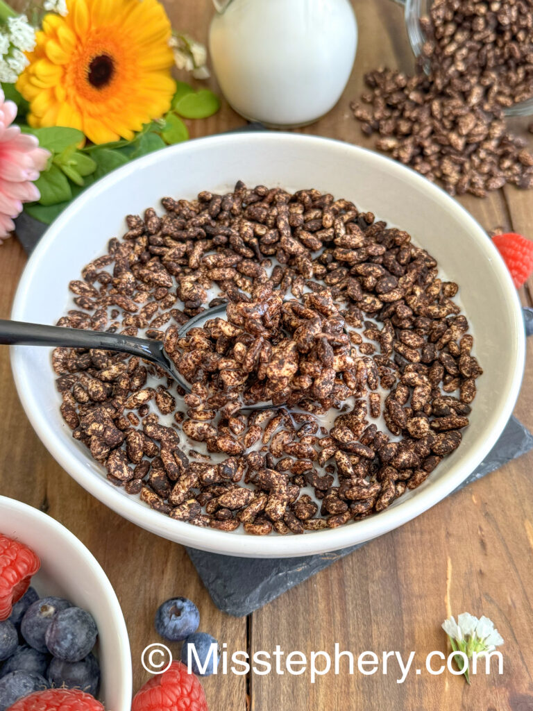 Une cuillère noire soulevant une bouchée croustillante de riz soufflé au chocolat maison saines et de lait végétal dans le bol