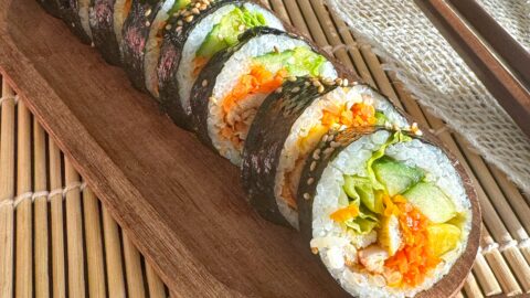 Kimbap au poulet gochujang et légumes frais sans gluten sur un plateau en bois.