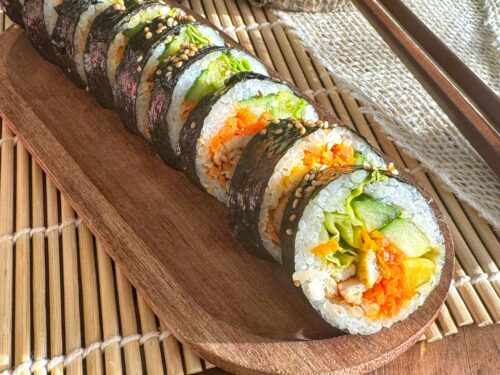 Kimbap au poulet gochujang et légumes frais sans gluten sur un plateau en bois.