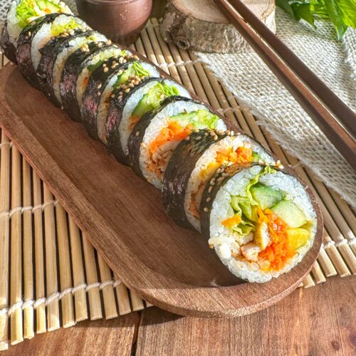 Kimbap au poulet gochujang et légumes frais sans gluten sur un plateau en bois.