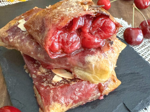 Chaussons aux cerises croustillants sans gluten et sans lactose faits avec des feuilles de riz, présentés sur une ardoise avec un tournesol.