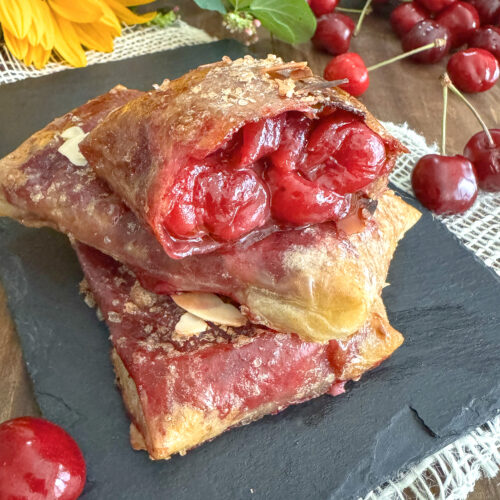 Chaussons aux cerises croustillants sans gluten et sans lactose faits avec des feuilles de riz, présentés sur une ardoise avec un tournesol.
