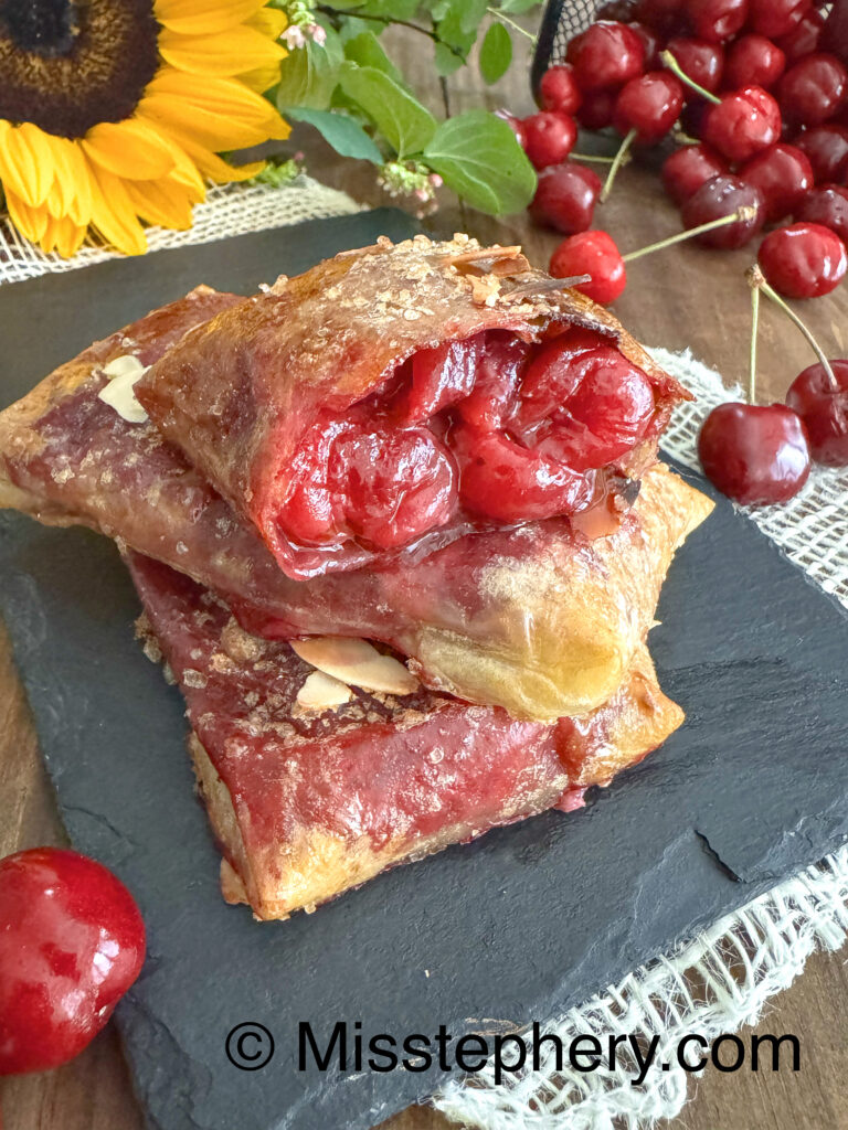 Chaussons aux cerises croustillants sans gluten et sans lactose faits avec des feuilles de riz, présentés sur une ardoise avec un tournesol.