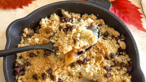 Une bouchée de crumble végétalien aux poires et pépites de chocolat, dessert d'automne servi chaud dans une mini poêle en fonte sur un fond décoratif de feuilles et de fruits.