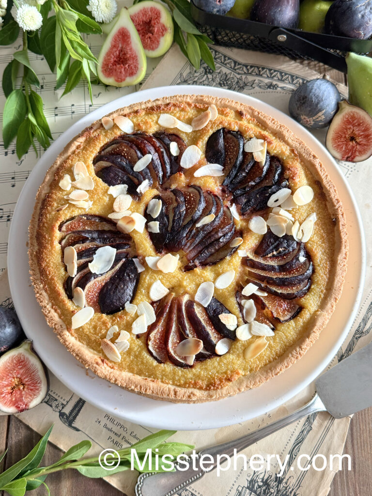 Vue du dessus d'une tarte amandine aux figues fraîches et amandes effilées, sans gluten et sans lactose, présentée dans un plat blanc.