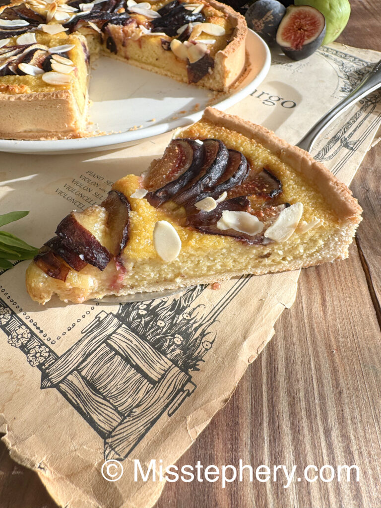 Gros plan sur une part de tarte aux figues et crème d'amande sans gluten ni lactose, posée sur un papier ancien imprimé.