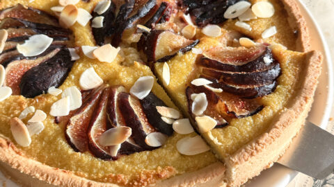 Une part de tarte amandine aux figues fraîches soulevée sur une pelle à gâteau argentée, montrant la texture moelleuse de la crème d'amande.