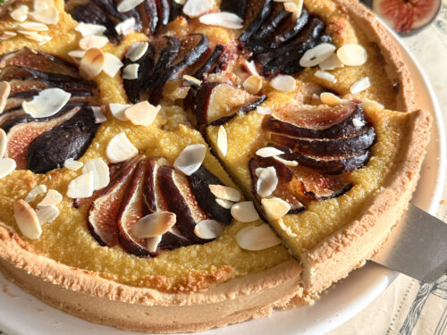 Une part de tarte amandine aux figues fraîches soulevée sur une pelle à gâteau argentée, montrant la texture moelleuse de la crème d'amande.