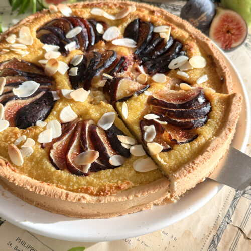 Une part de tarte amandine aux figues fraîches soulevée sur une pelle à gâteau argentée, montrant la texture moelleuse de la crème d'amande.