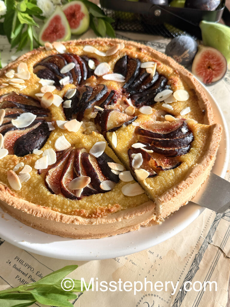 Une part de tarte amandine aux figues fraîches soulevée sur une pelle à gâteau argentée, montrant la texture moelleuse de la crème d'amande.
